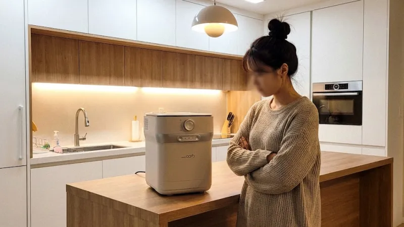 주방에 놓인 음식물처리기 옆에서 고민하는 여성의 옆모습